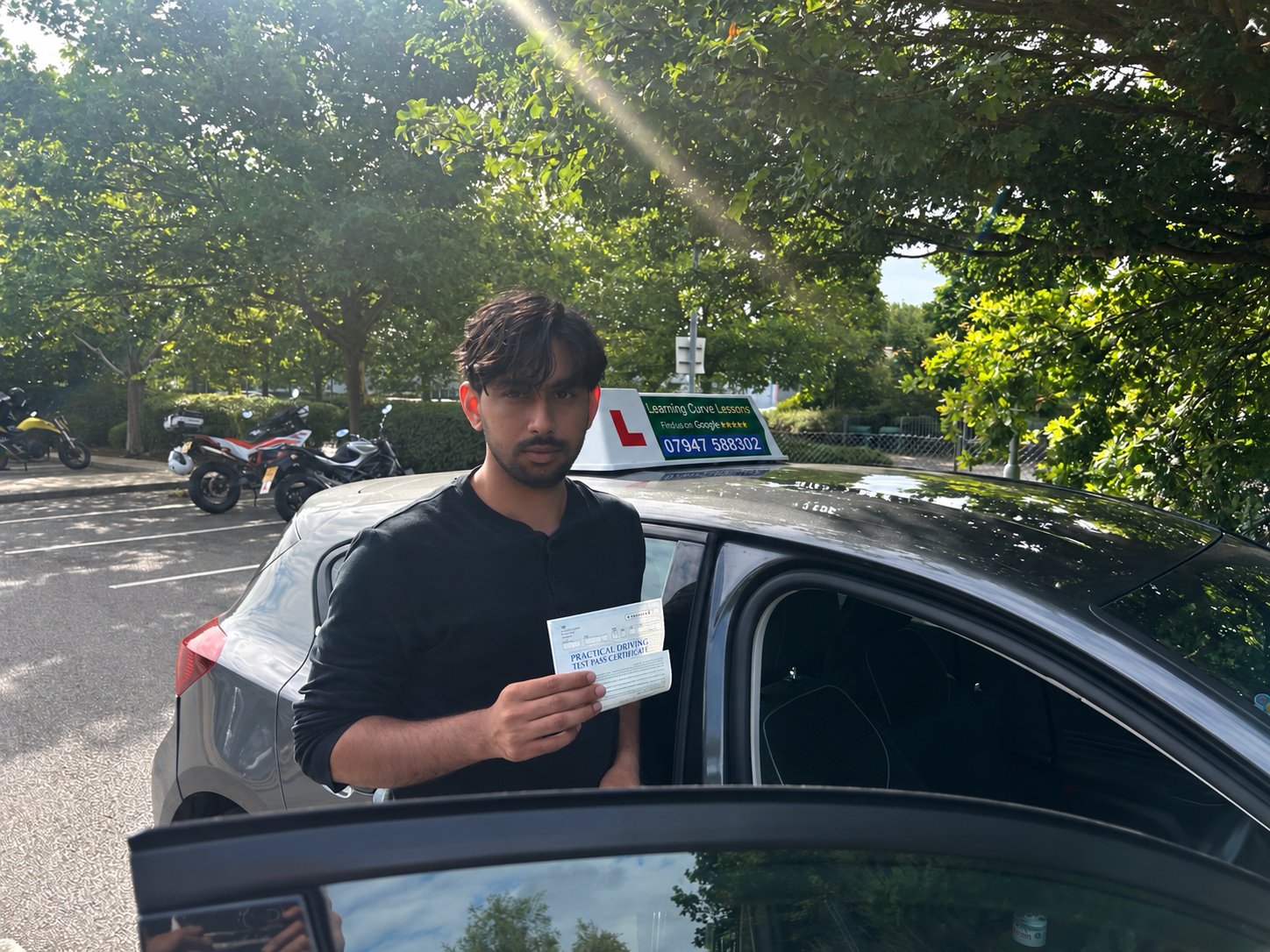 Pupil holding a driving test pass certificate beside a car with a Learning Curve roof sign